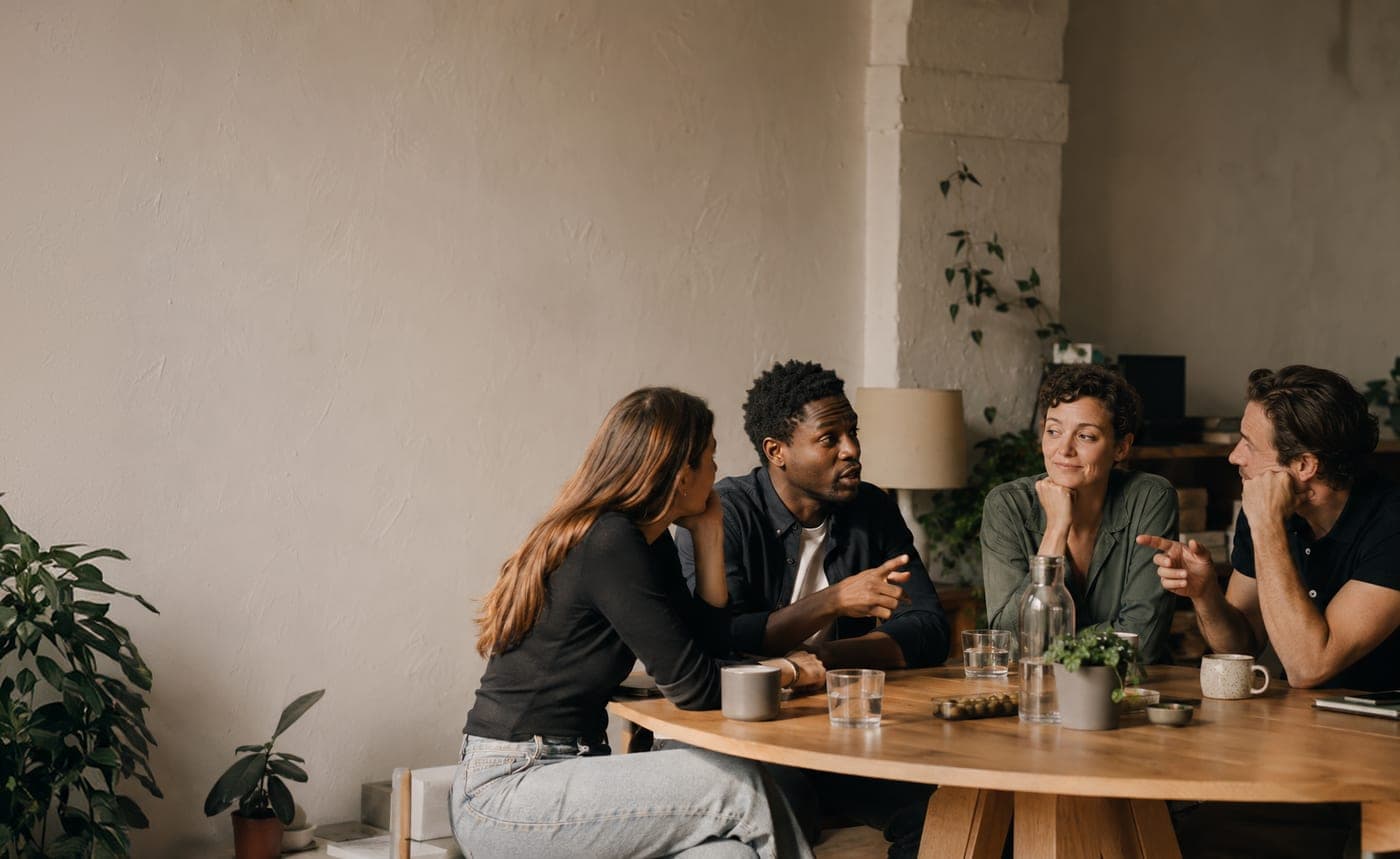 A group of friends gathered around a wooden table in a sunlit living room.